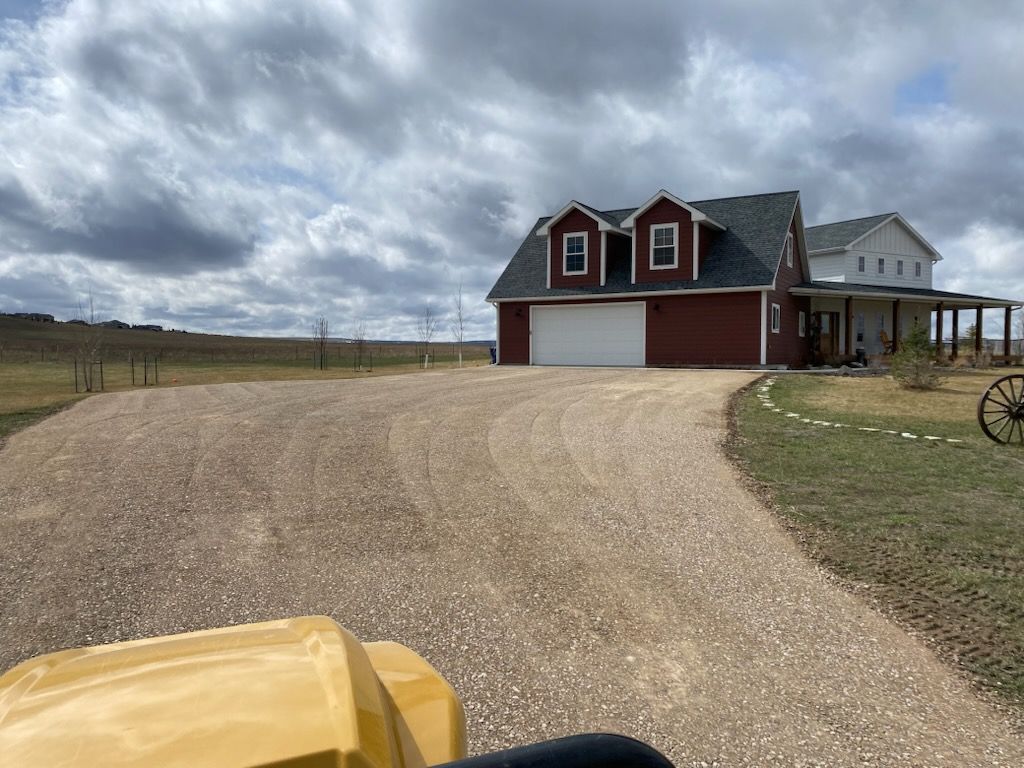 Vehicle tire tracks cut through a dirt landscape under a large tree casting a long shadow on a sunny day.