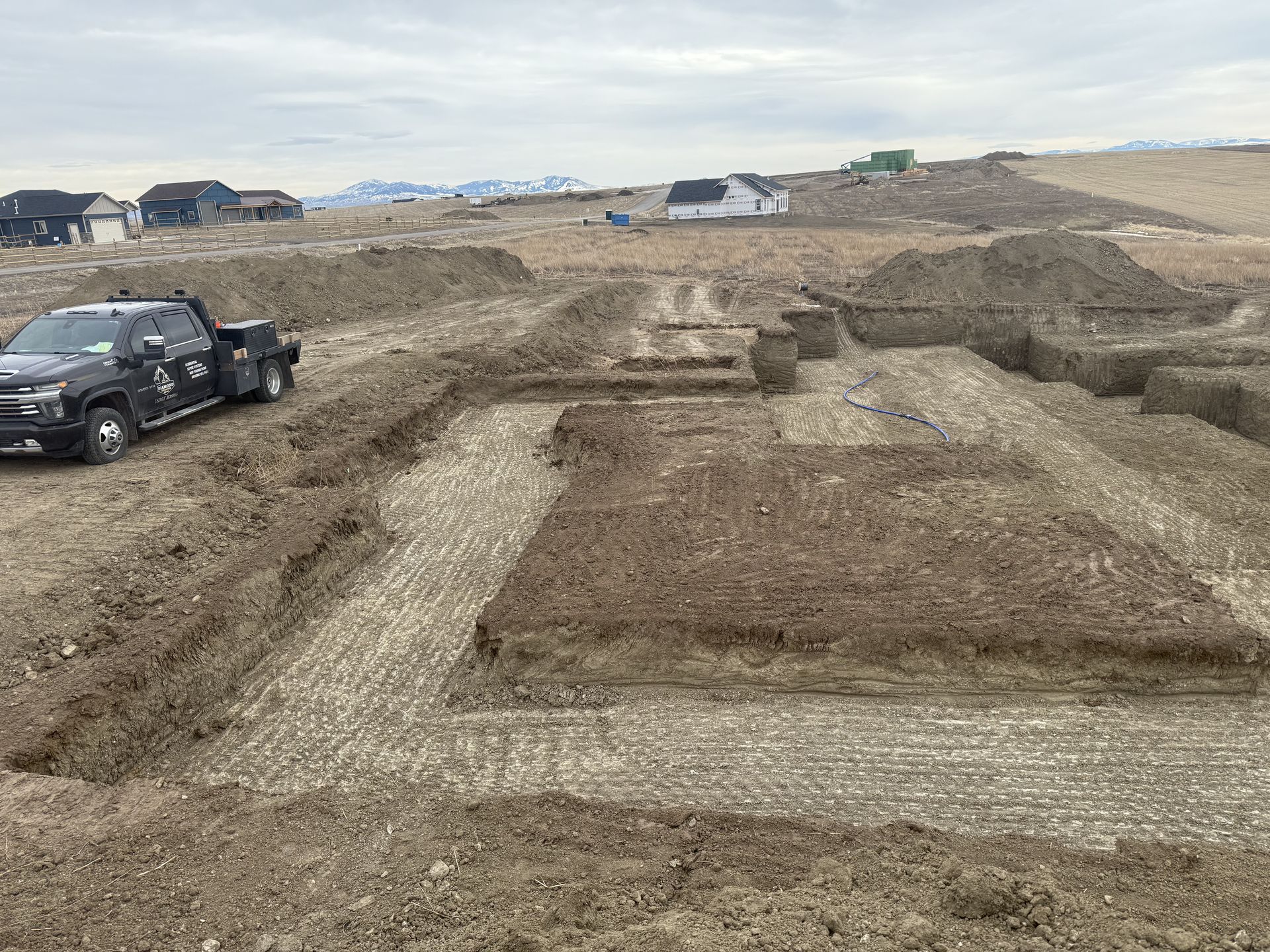 A black pickup truck parked next to a large, newly excavated foundation trench for a house in an open, rural landscape.