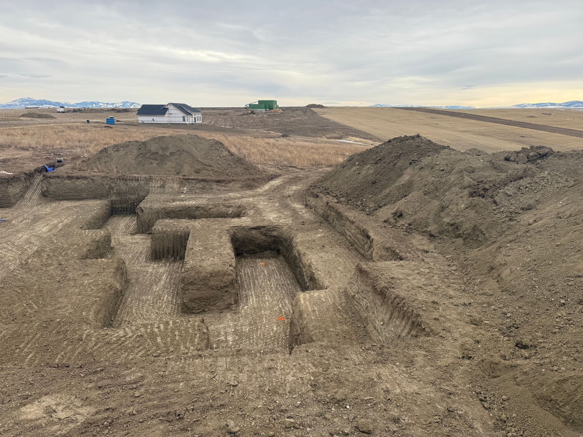 A construction site with excavated foundation trenches in the dirt under a cloudy sky.