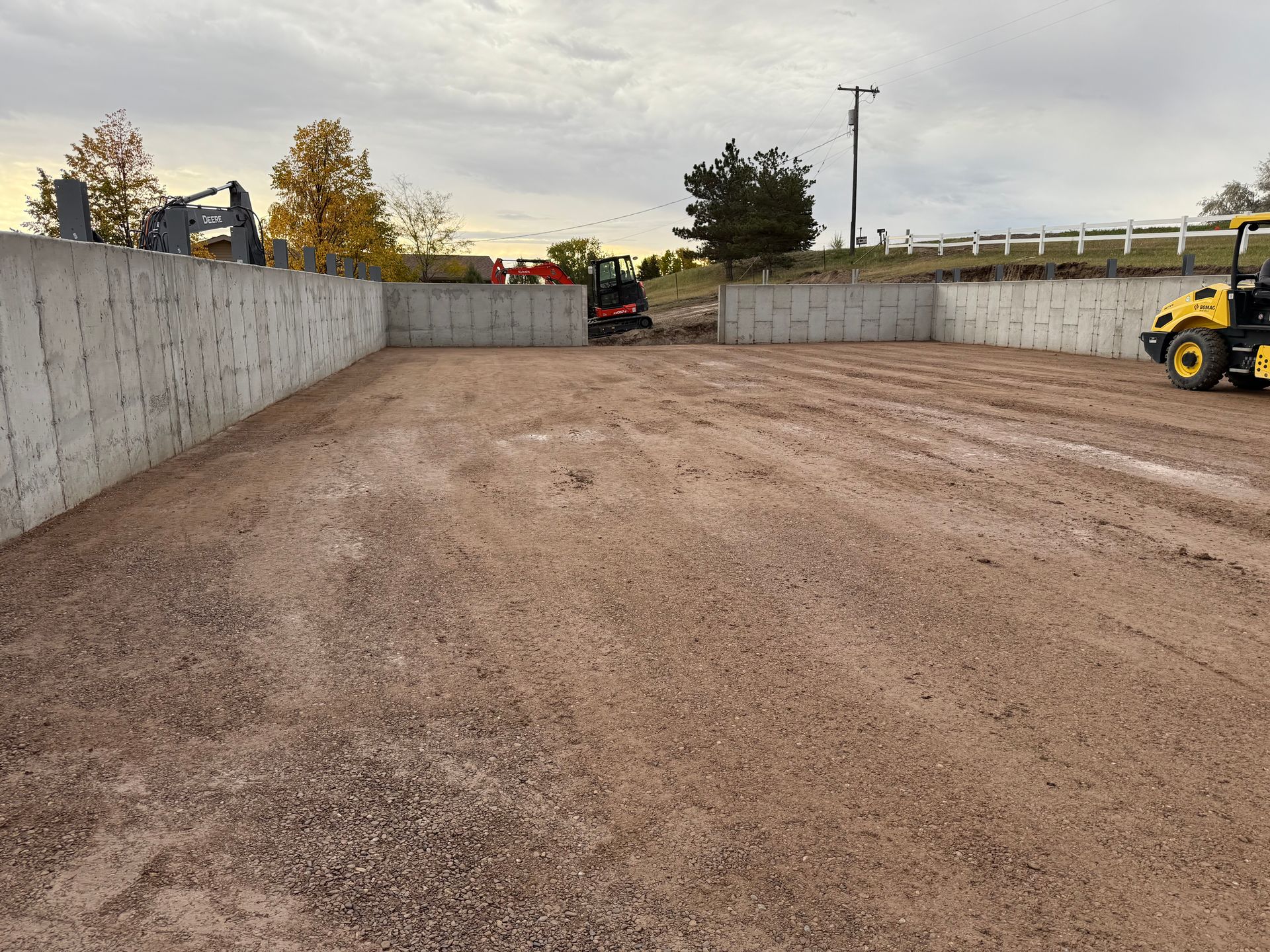 A construction site with concrete foundation walls forming a U-shape around a gravel ground area, with heavy machinery.