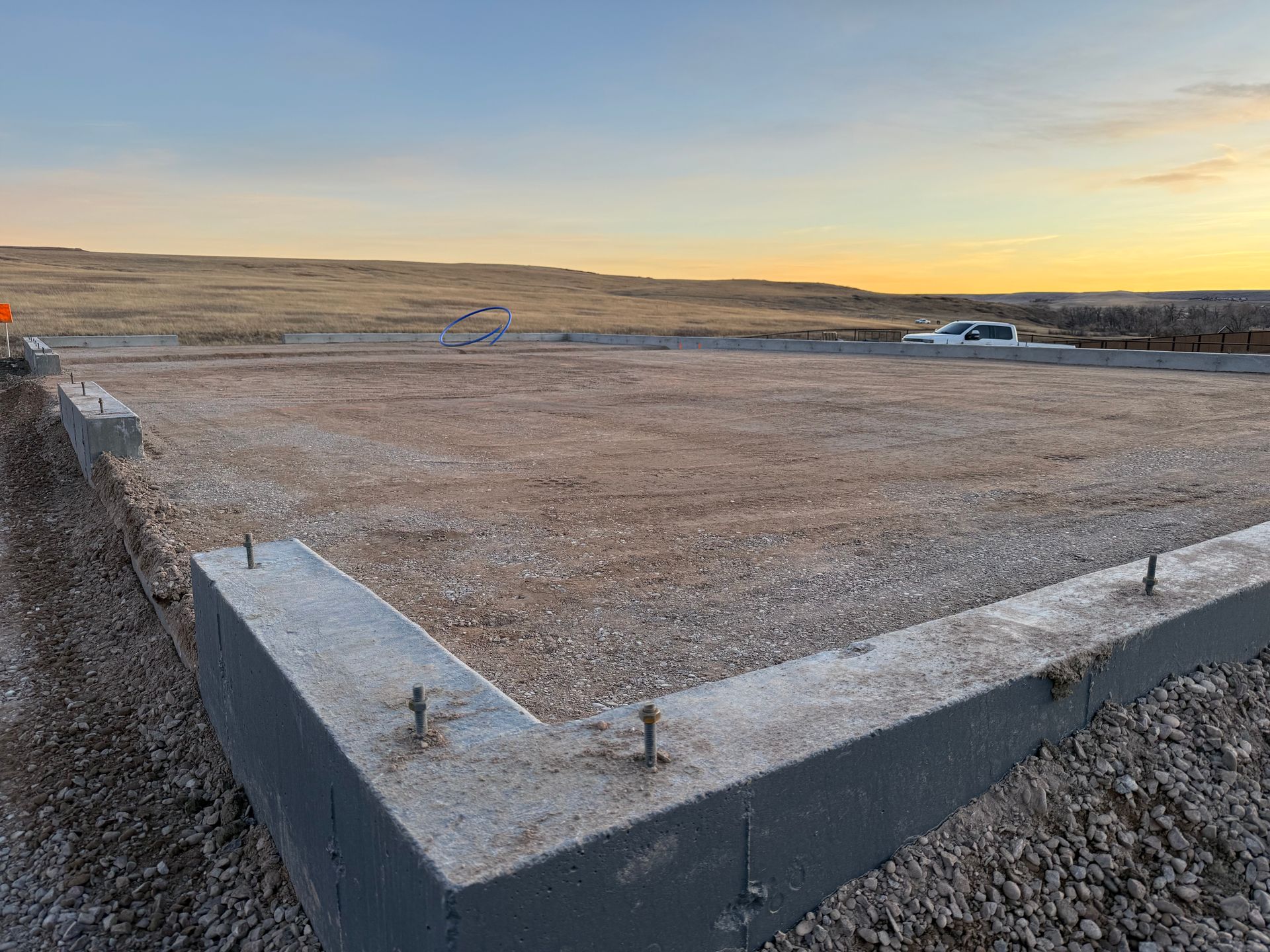 A concrete foundation for a building under construction at sunset, featuring anchor bolts embedded in the perimeter wall.