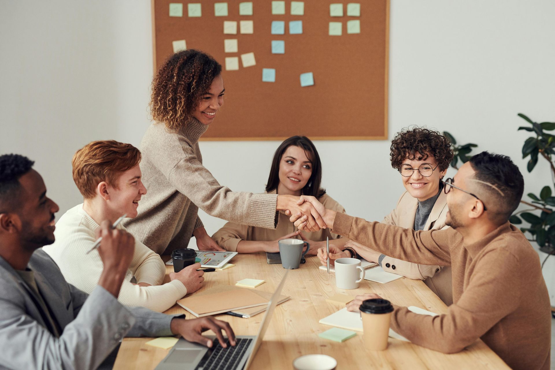 A group of people are sitting around a table shaking hands.