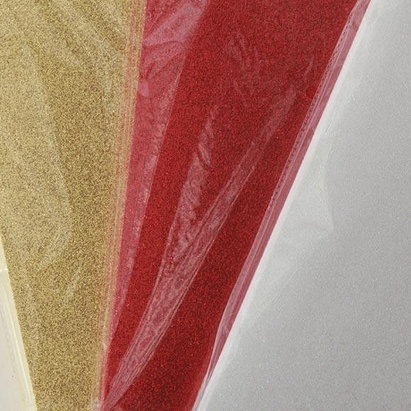 Primer plano de tres hojas de colores: dorada, roja y blanca, cada una envuelta en plástico transparente.