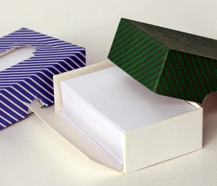 Tarjetas blancas apiladas en una caja blanca, con una tapa de caja estampada en verde y azul al lado.