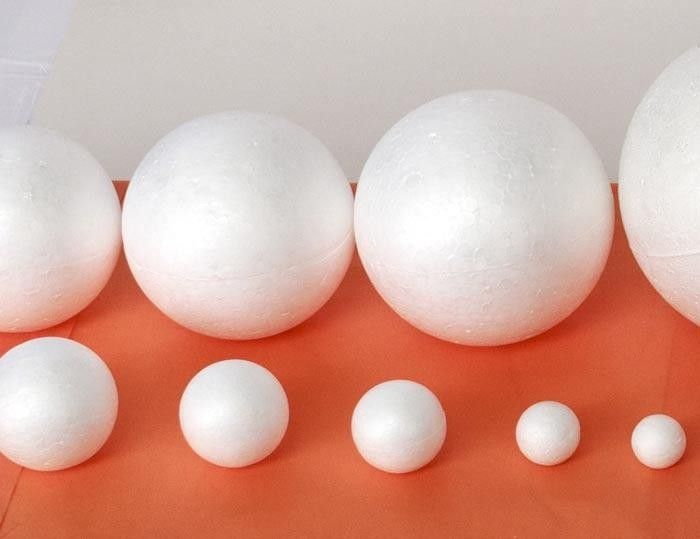 Hilera de bolas de poliestireno blancas de diferentes tamaños sobre una superficie naranja.