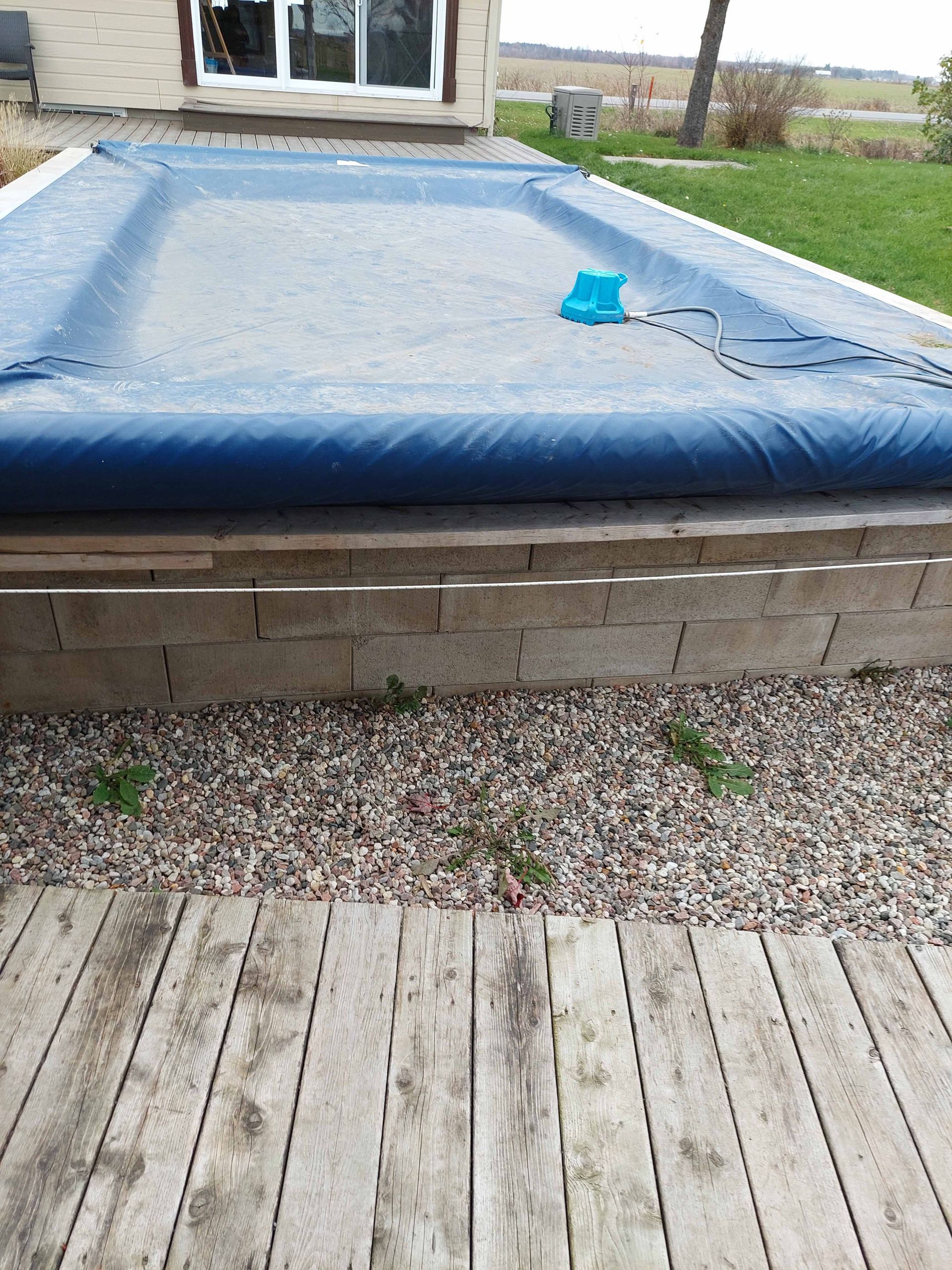 A large swimming pool is surrounded by potted plants and a wooden deck.