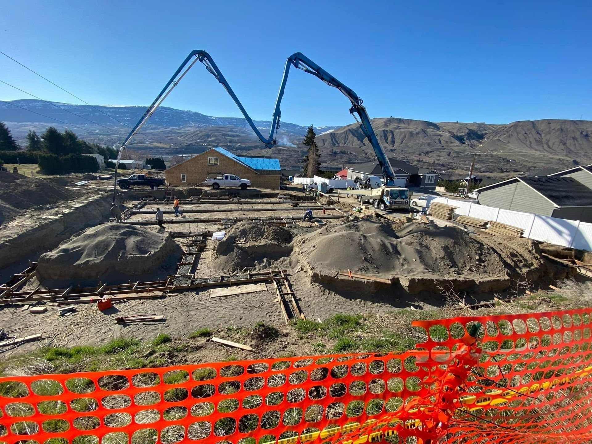 Construction site with concrete pump trucks pouring concrete into foundation forms under a blue sky.