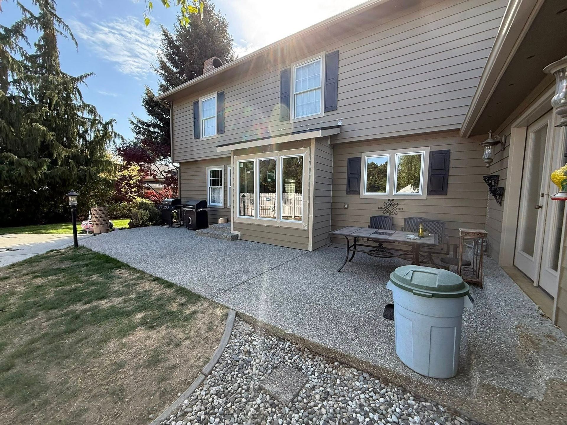 Beige house with a gravel patio, outdoor seating, and a large green trash can.