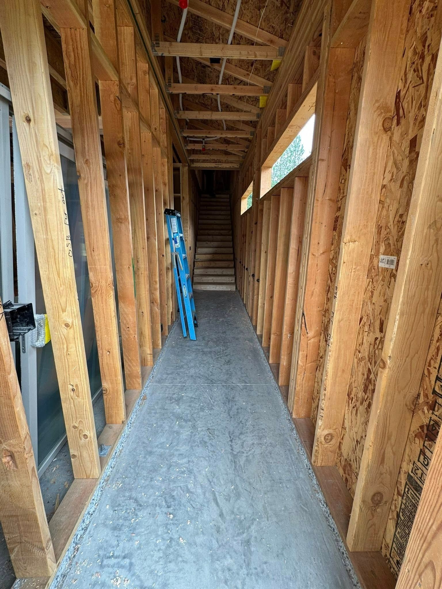 Unfinished interior hallway with wood framing, gravel floor, and a ladder leaning against a wall.