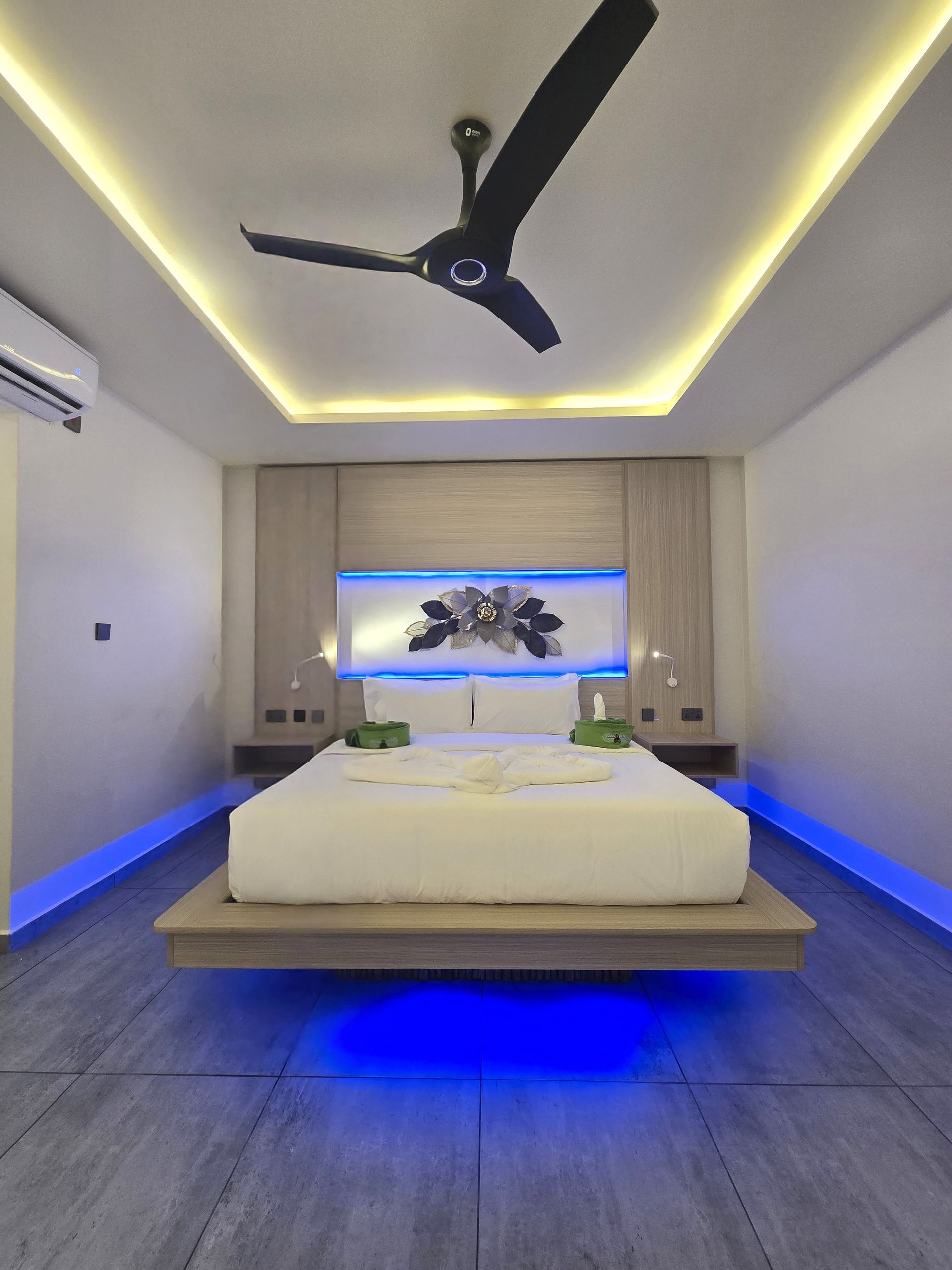 Modern bedroom with a floating bed, blue underlighting, and a ceiling fan.
