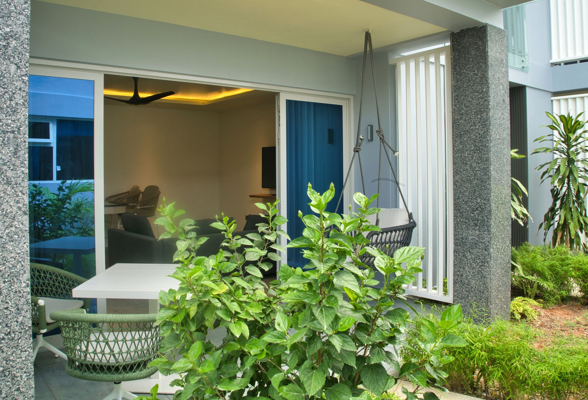 Patio with sliding glass door, swing, and outdoor table with lush greenery. Interior living space visible.