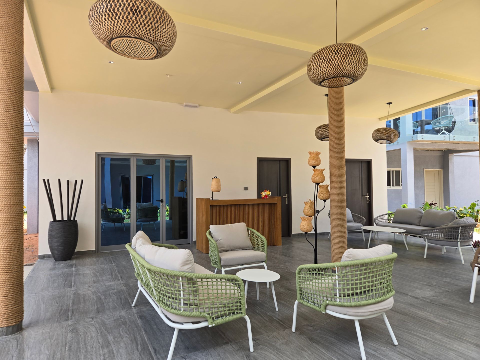 Outdoor lounge area with light green wicker furniture, gray sofas, and decorative rope columns.