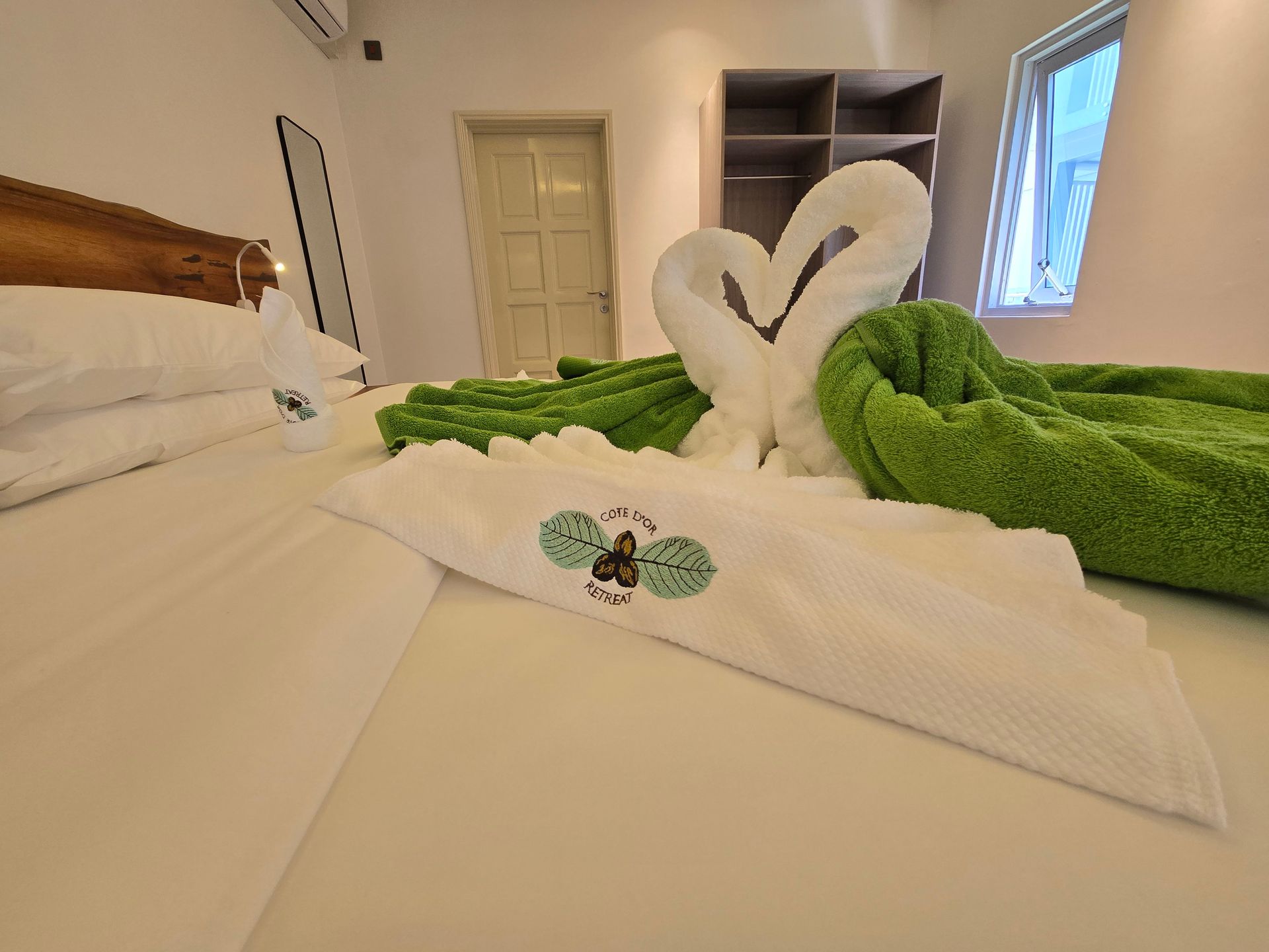 Bedroom with swan towel art on bed; green and white towels, open closet, window.