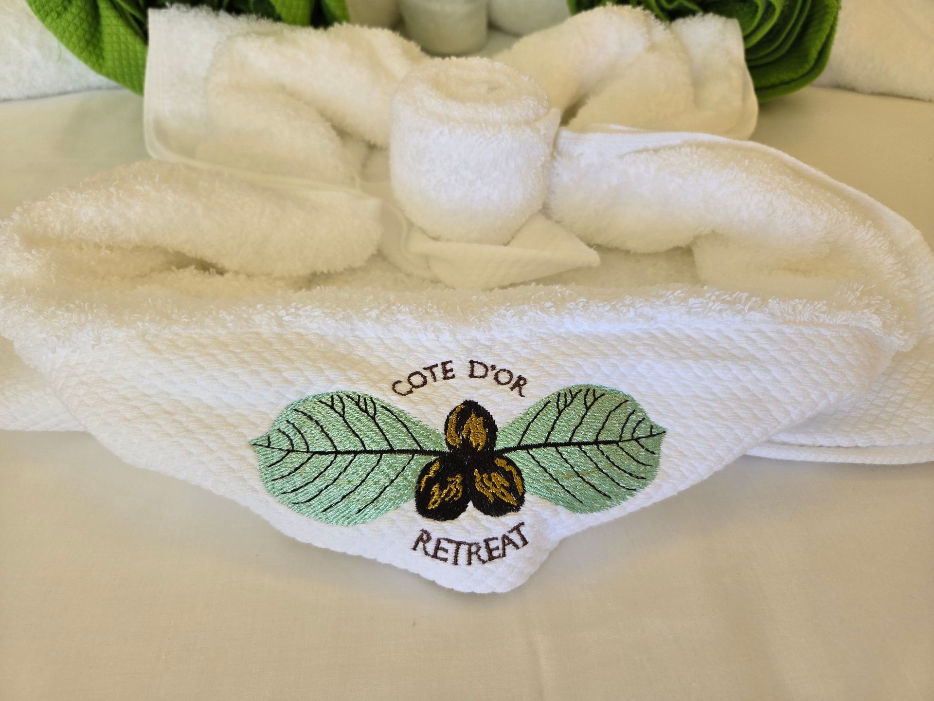 White towel folded in the shape of a flower with “Cote d’Or Retreat” logo embroidered.