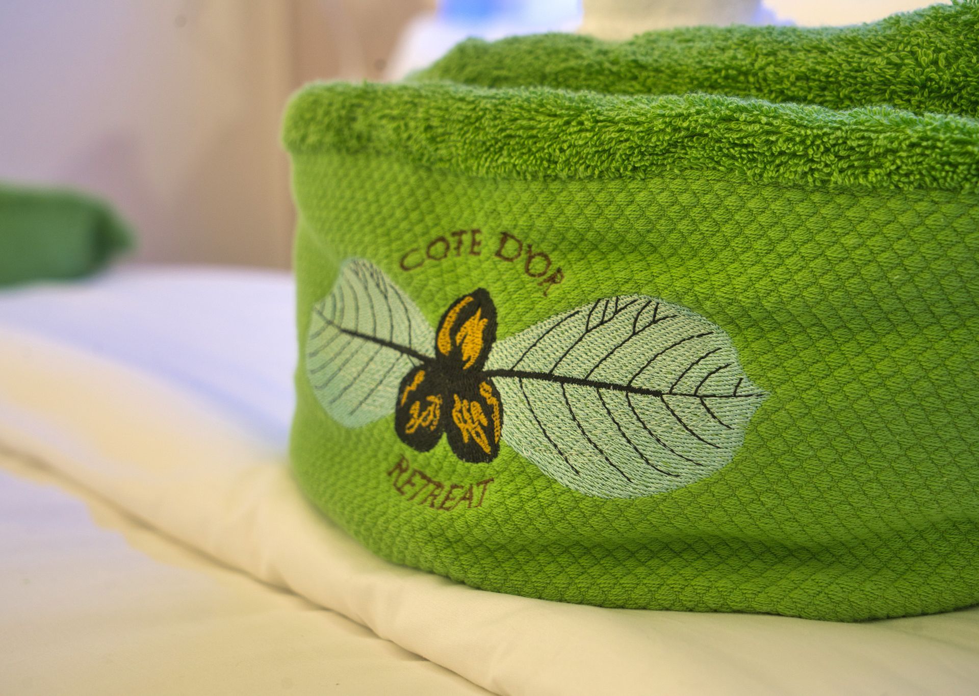 Green towel, embroidered logo, folded on white linens. 