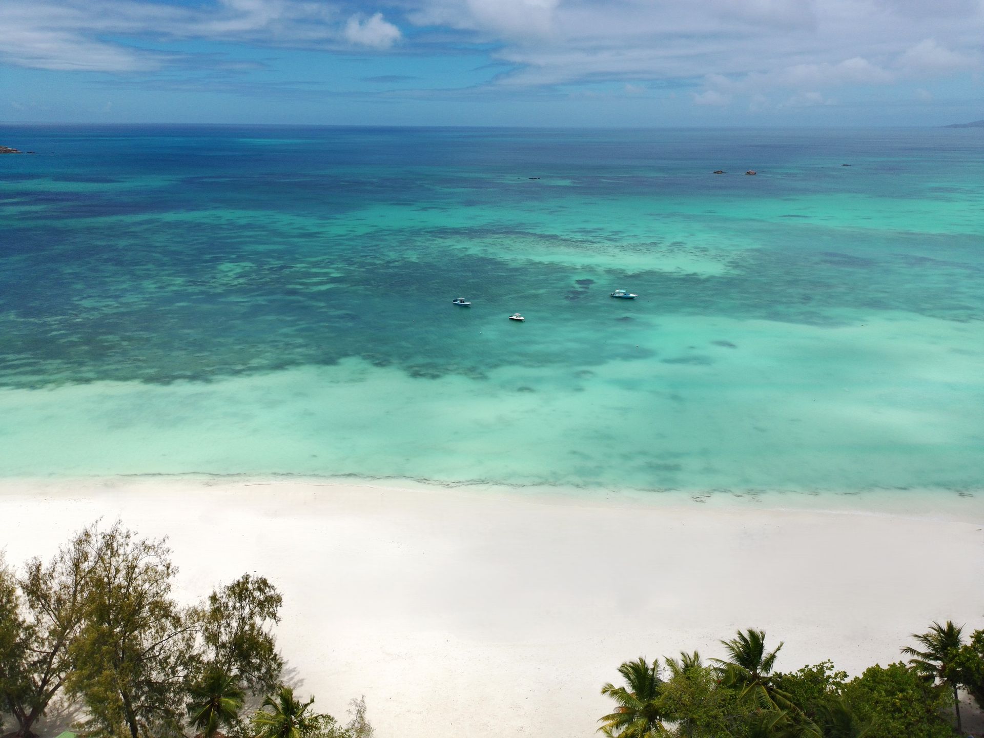 White sand beach meets turquoise ocean, boats scattered in the water, under a blue sky.