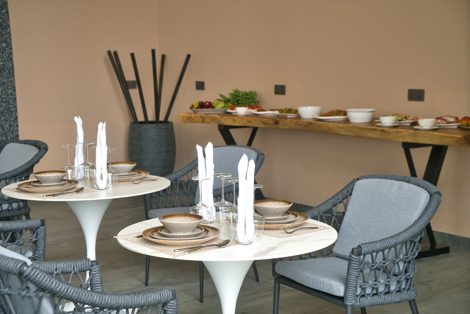 Outdoor dining area with tables set for a meal. Buffet table with food in background.