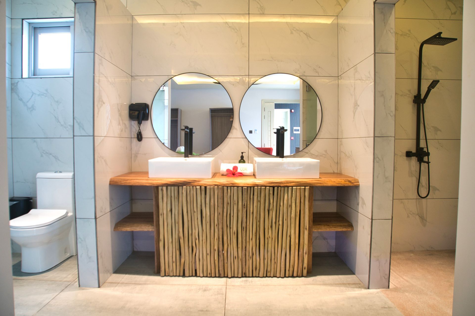 Bathroom with double sinks, round mirrors, wooden vanity, toilet, and shower.