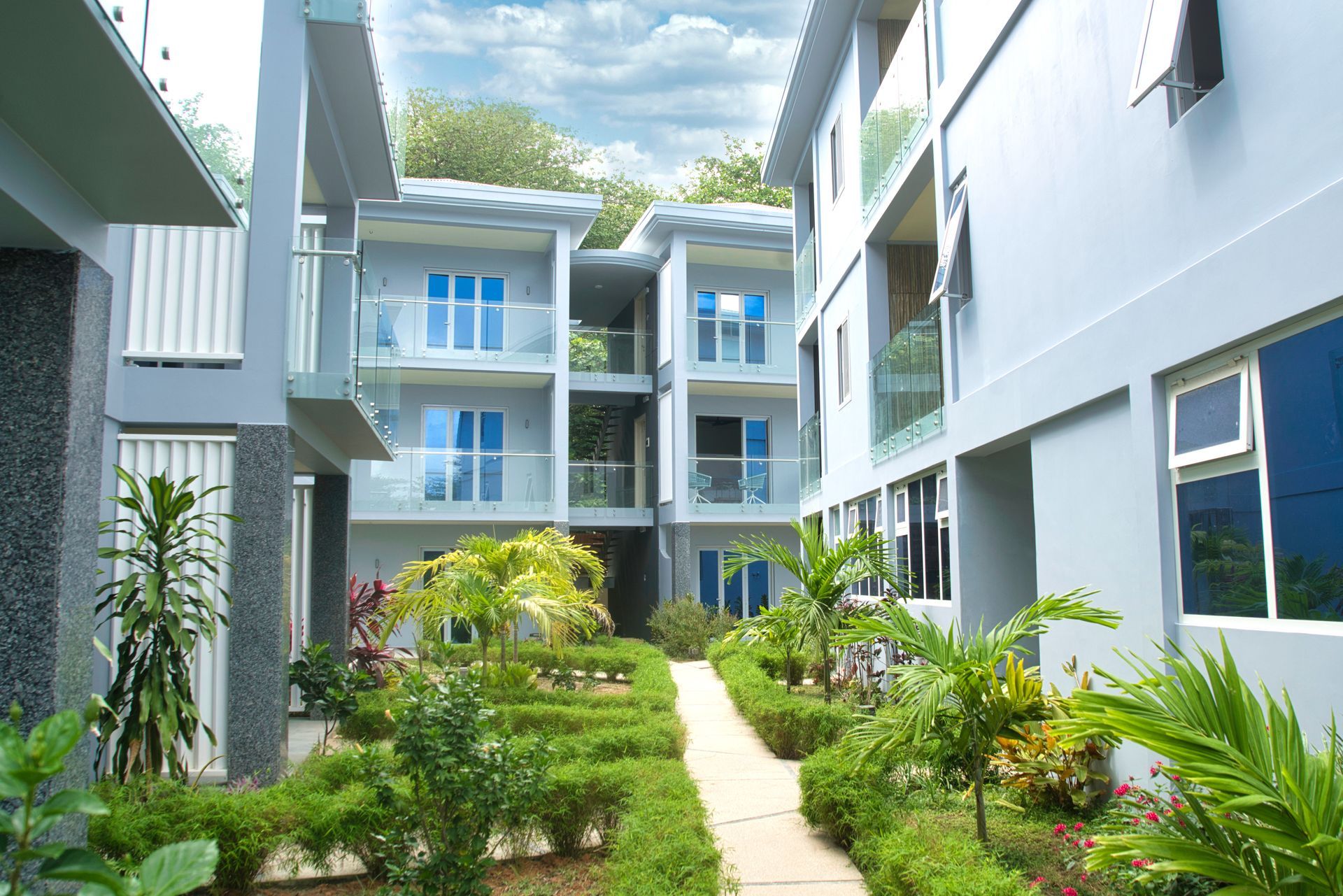 Exterior of modern, gray apartments with balconies, glass railings, and a small garden.