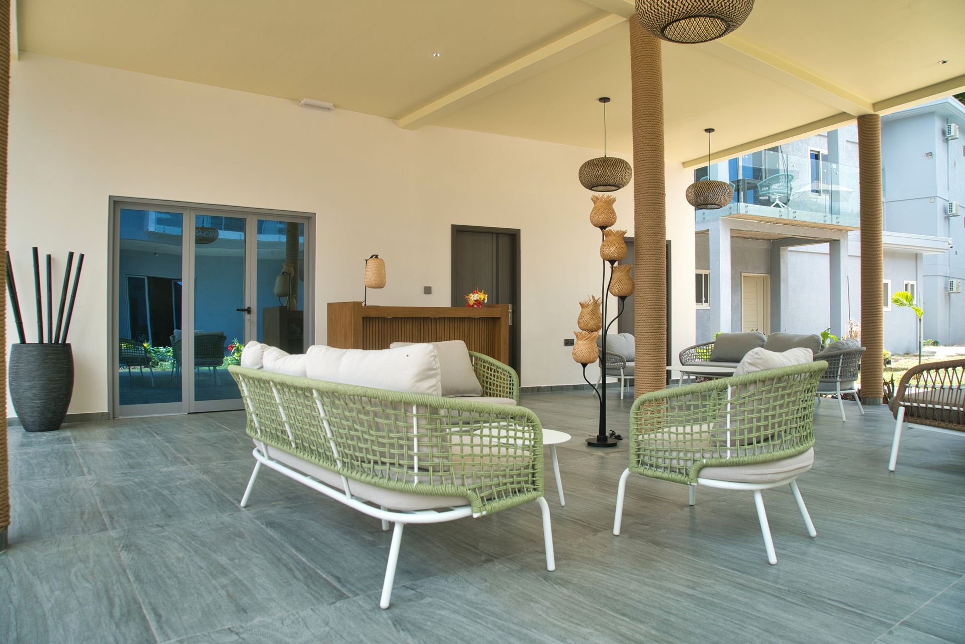 Outdoor lounge area with green woven sofas and chairs, gray flooring, and decorative hanging lights.