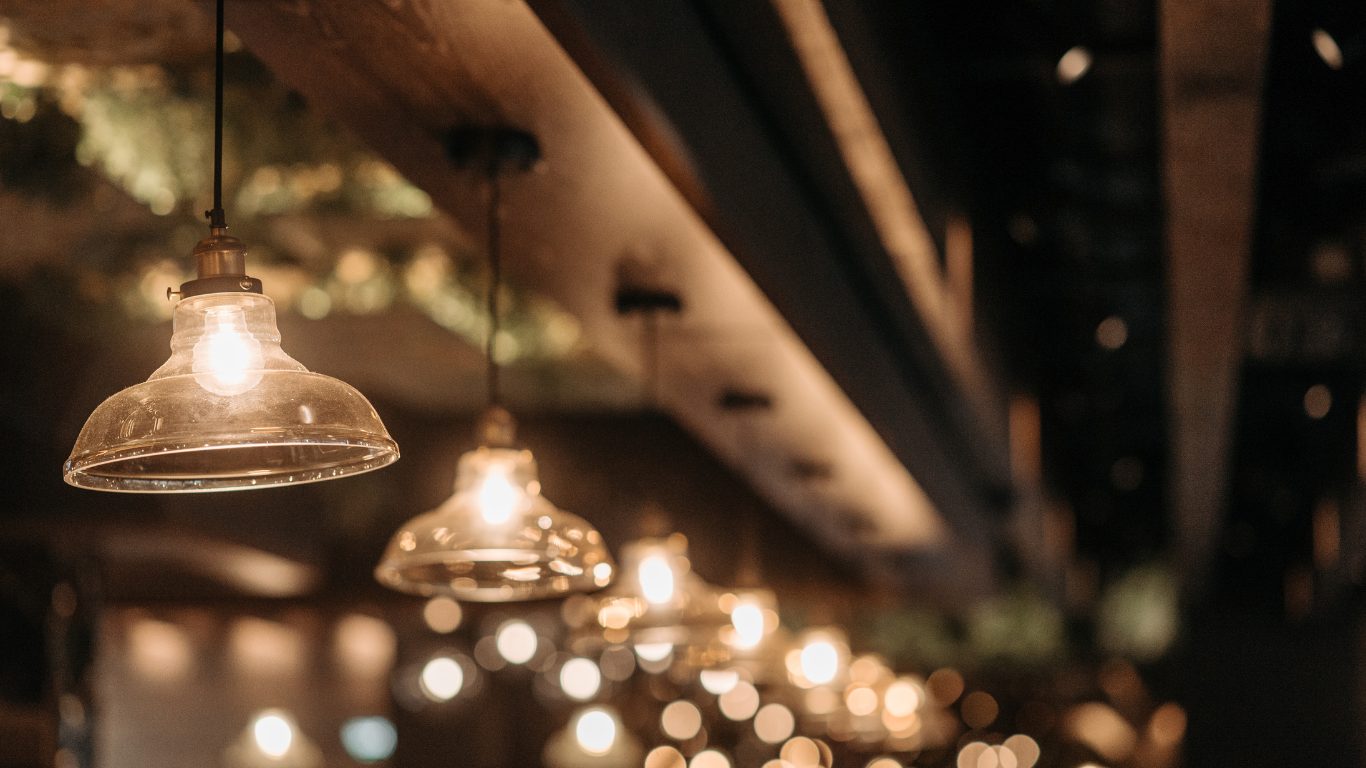 A row of glowing pendant lights hanging from a wooden beam in a dimly lit, blurred interior space.