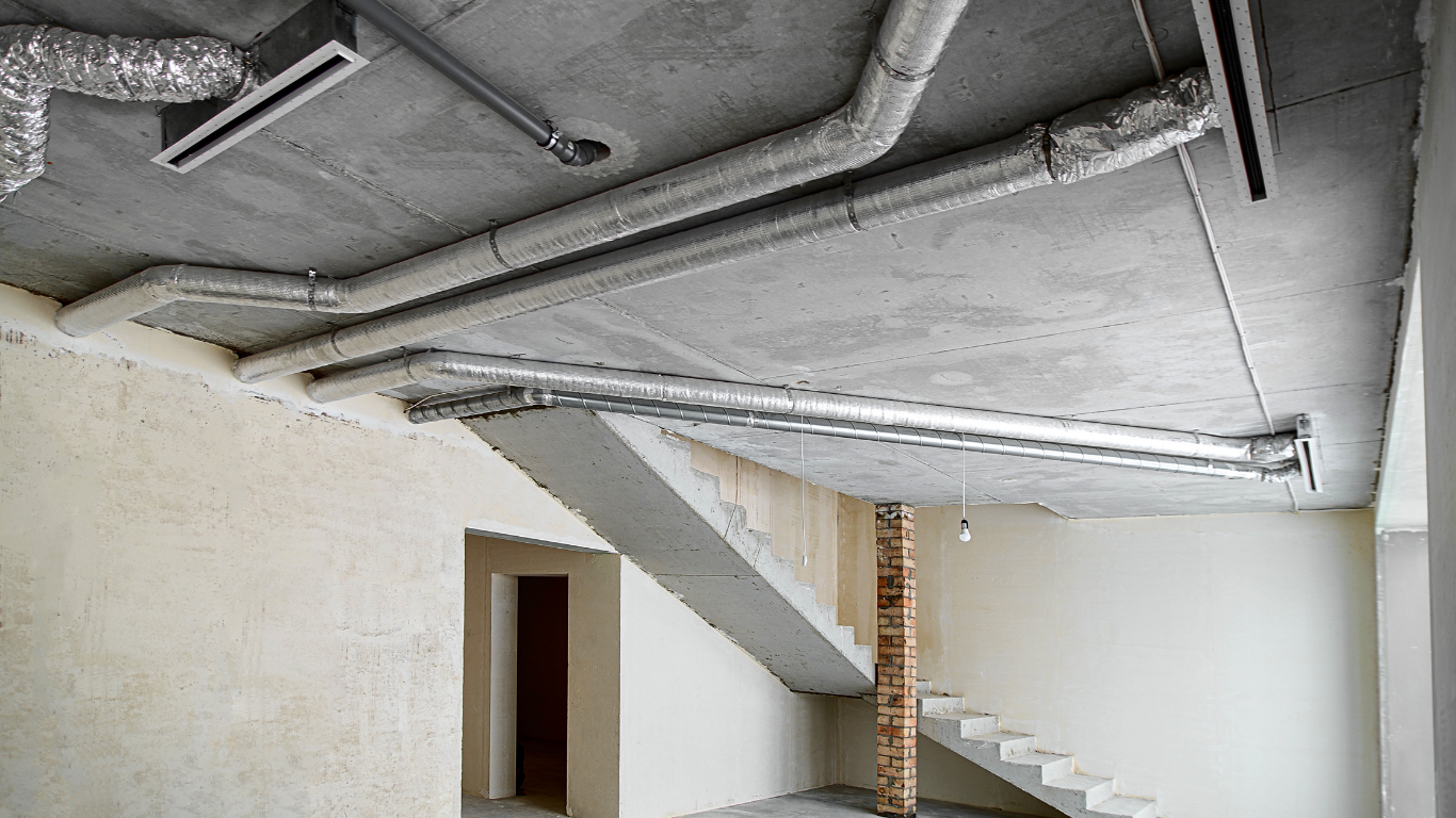 An unfinished interior room with a concrete ceiling featuring exposed metallic HVAC ducts and a concrete staircase.