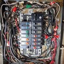 An open residential electrical breaker panel showing a cluttered arrangement of multicolored wiring and circuit breakers.