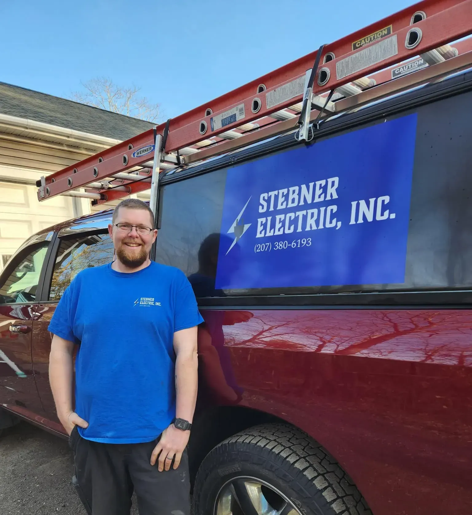 A person in a blue shirt standing beside a red service truck labeled Stebner Electric, Inc. with a ladder on the roof.
