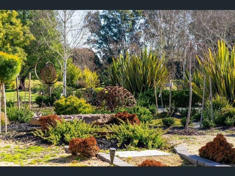 A landscaped garden featuring diverse green shrubs, tall ornamental grasses, and metal sculptural elements.
