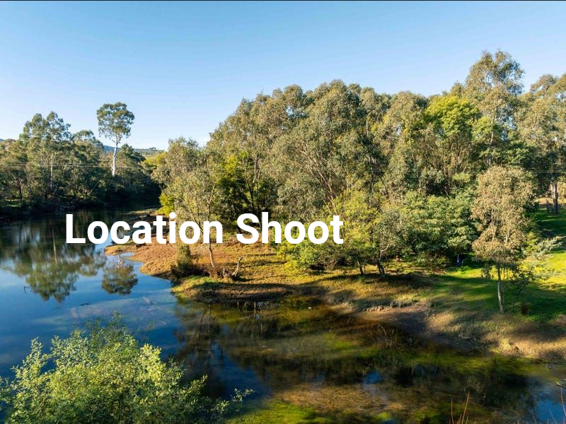 A calm river flows along a lush, tree-lined bank under a clear blue sky, with the text 