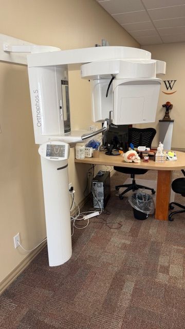 An x-ray machine is sitting in a room next to a desk.