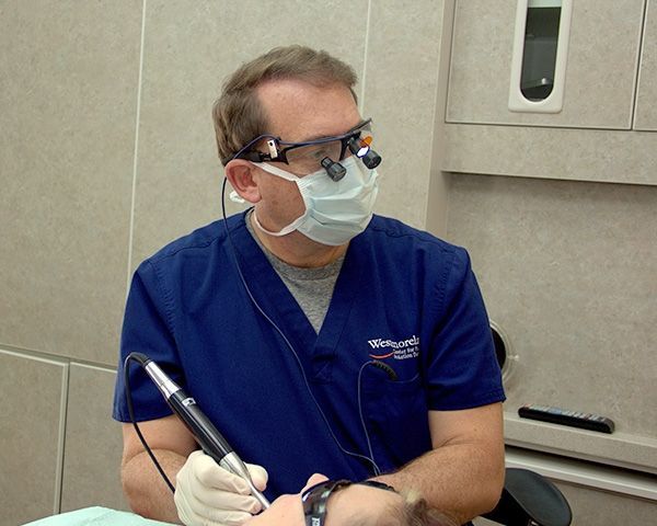 A dentist wearing a mask and glasses is working on a patient 's teeth