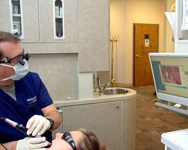 A dentist wearing a mask and glasses examines a patient 's teeth