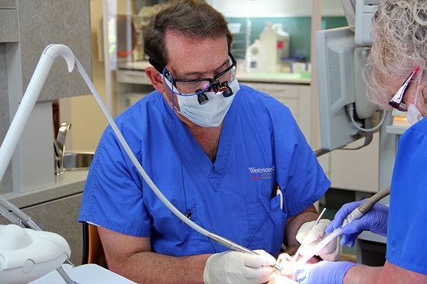 A dentist wearing a mask and glasses is working on a patient 's teeth