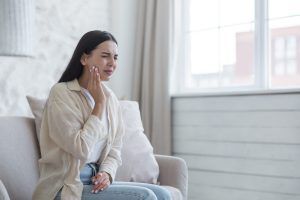 A woman is sitting on a couch with a toothache.