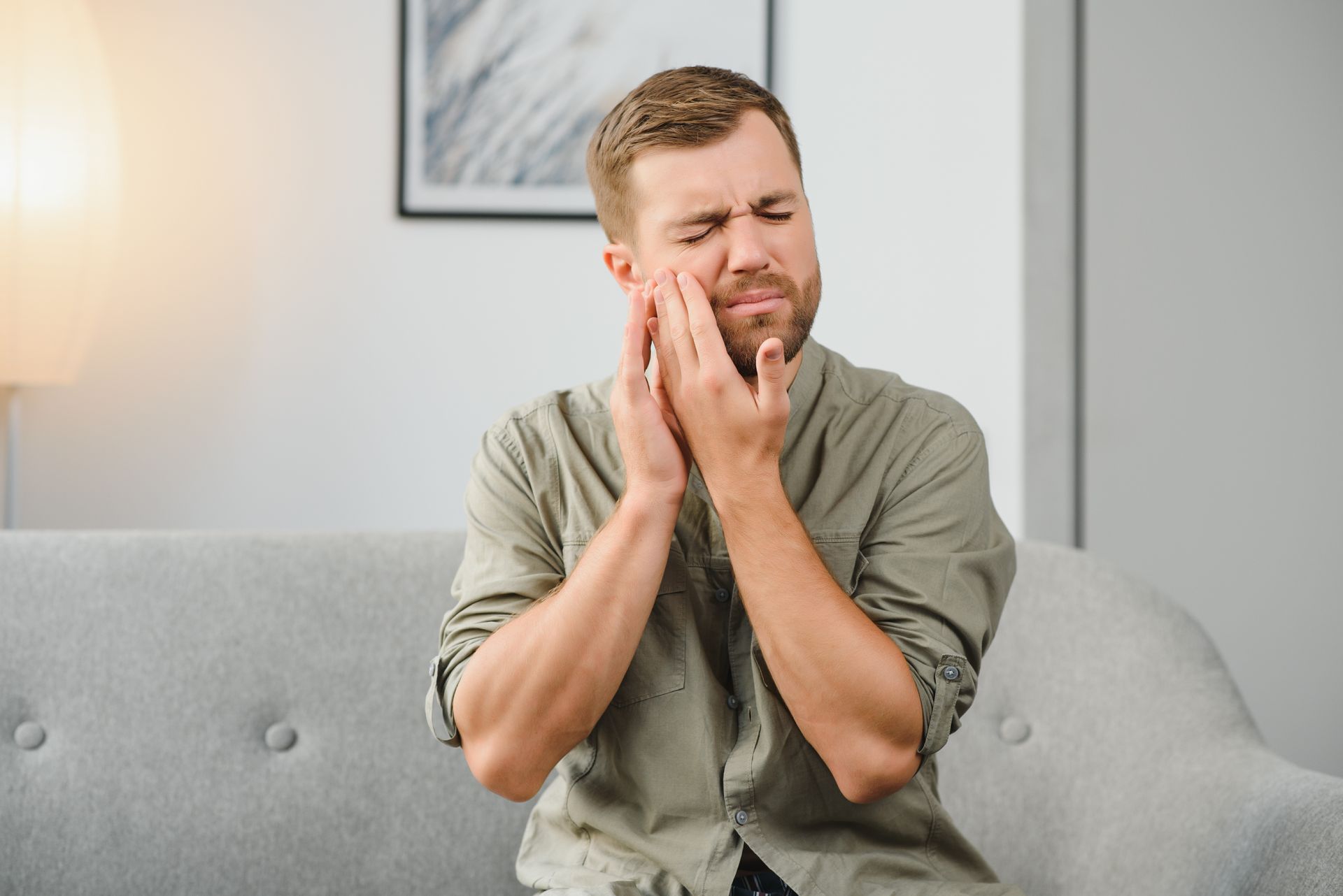 A man is sitting on a couch with a toothache.