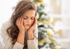 A woman is sitting in front of a christmas tree with her head in her hands.