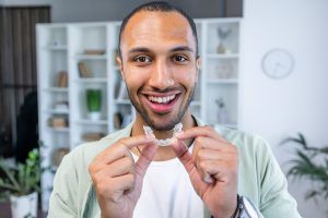 A man is holding a clear aligner in his hands and smiling.