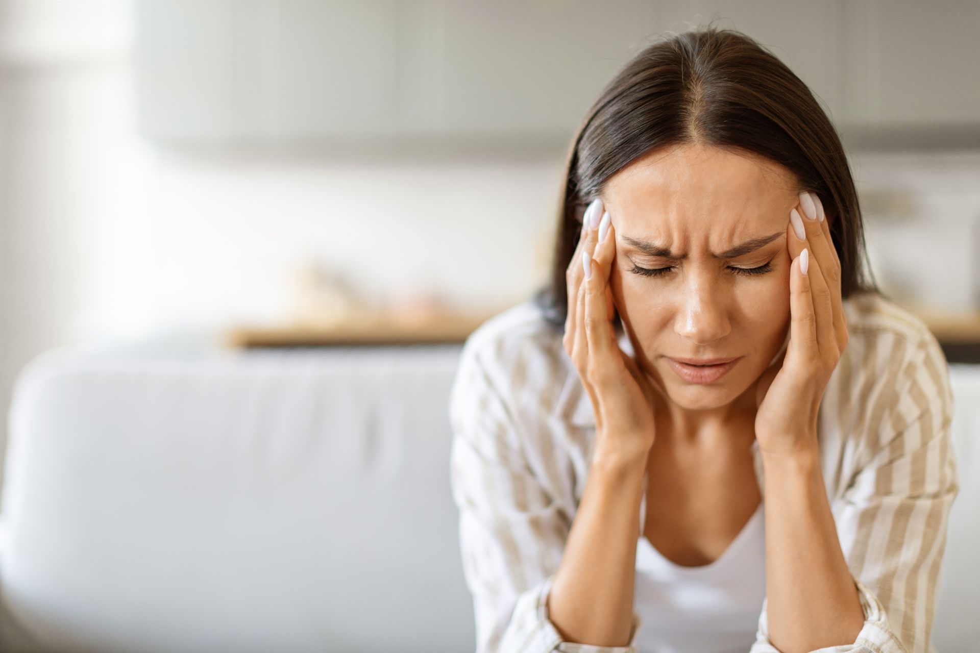 A woman is sitting on a couch with her hands on her head.