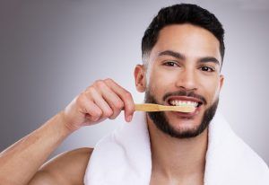 A man is brushing his teeth with a bamboo toothbrush.