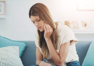 A woman is sitting on a couch with a toothache.