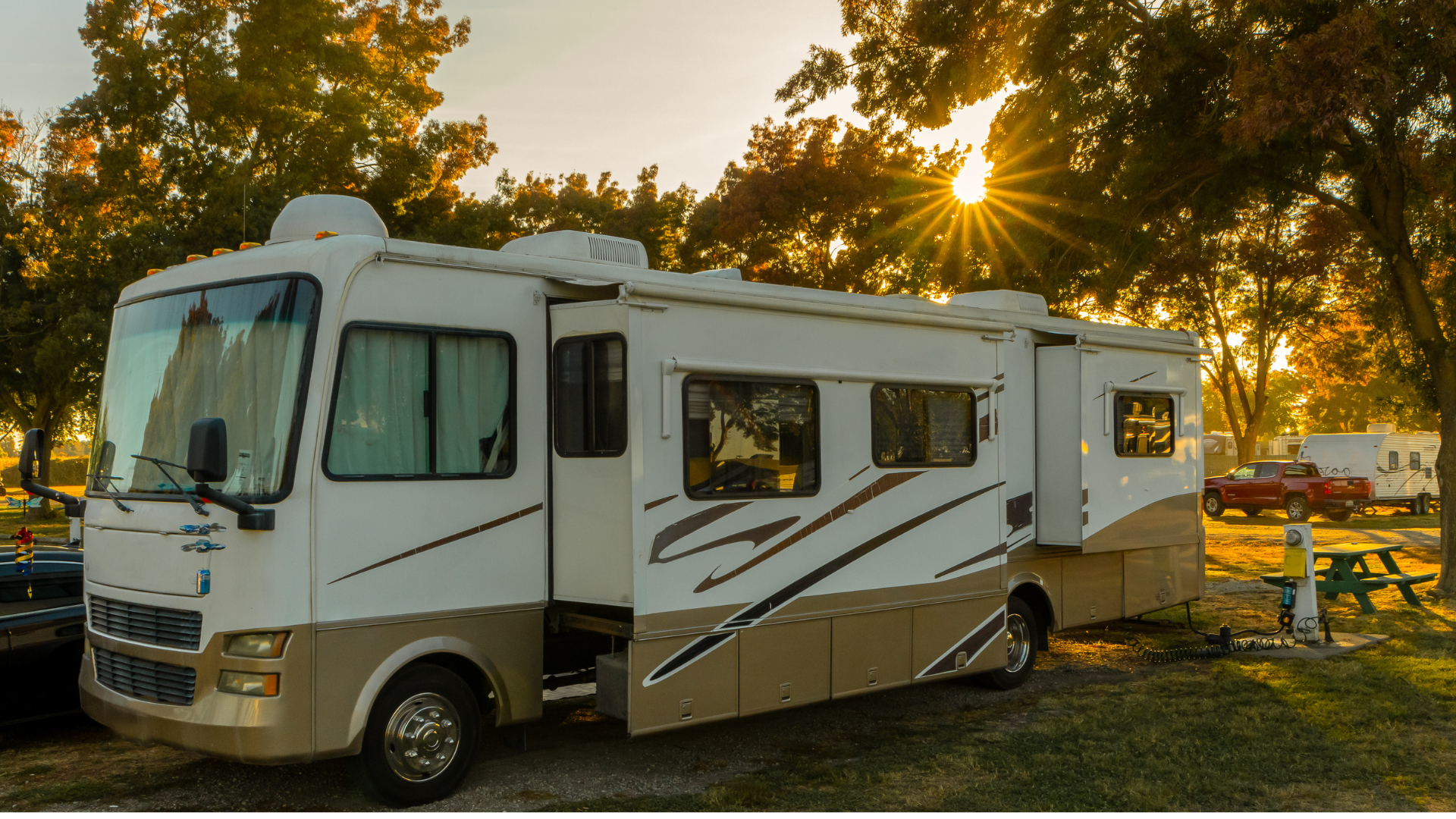 RV parked at a campsite, golden hour, sun shining through trees.