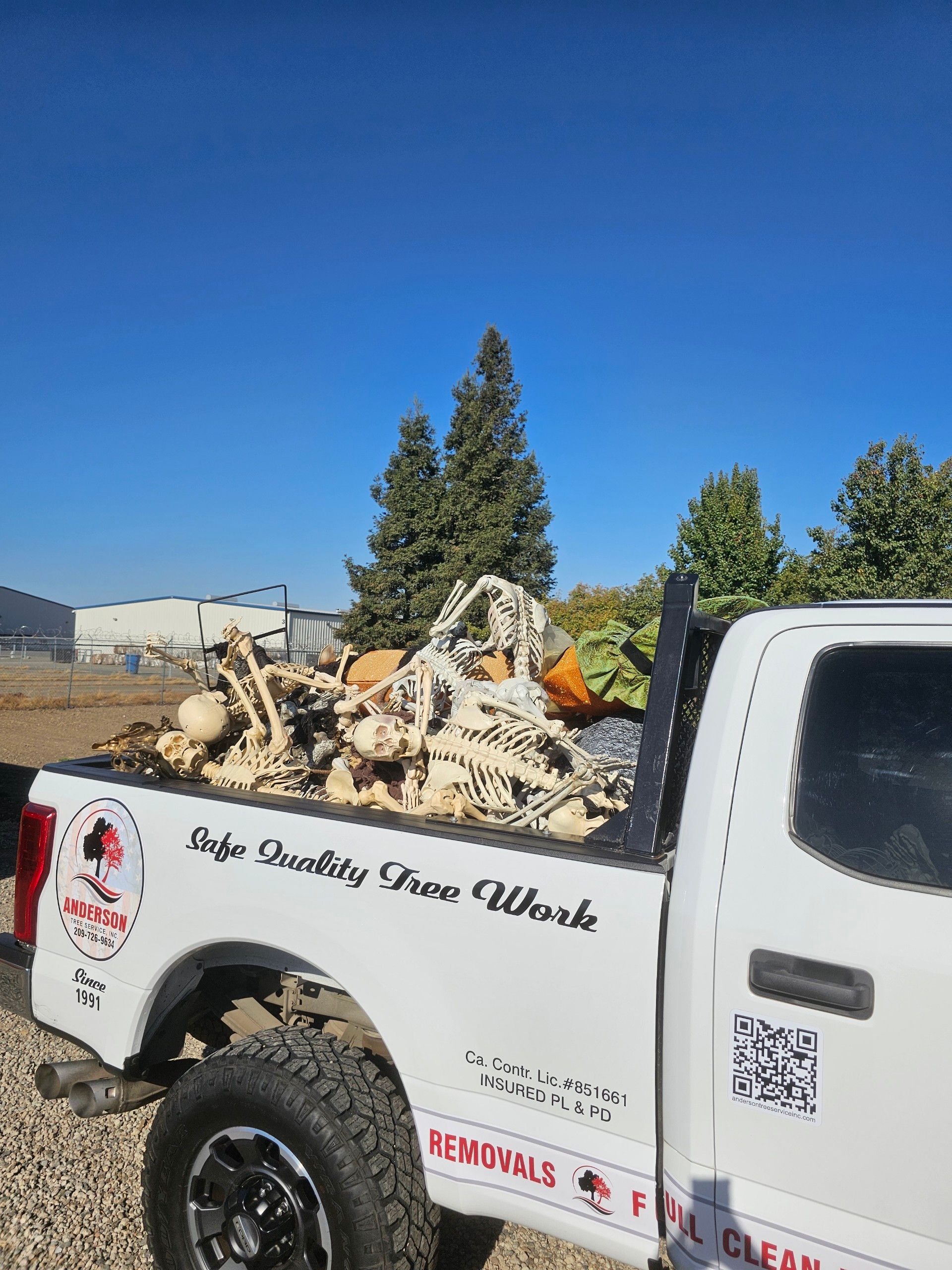 A white truck with a lot of wood in the back is parked in a gravel lot.