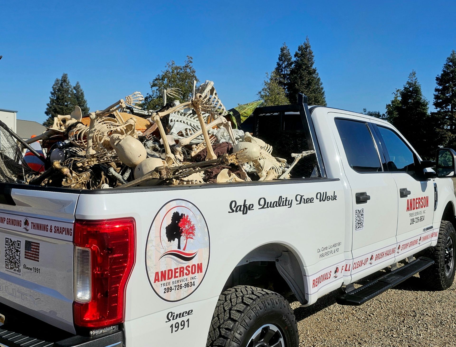 A white truck with a pile of wood in the back is parked on a gravel road.