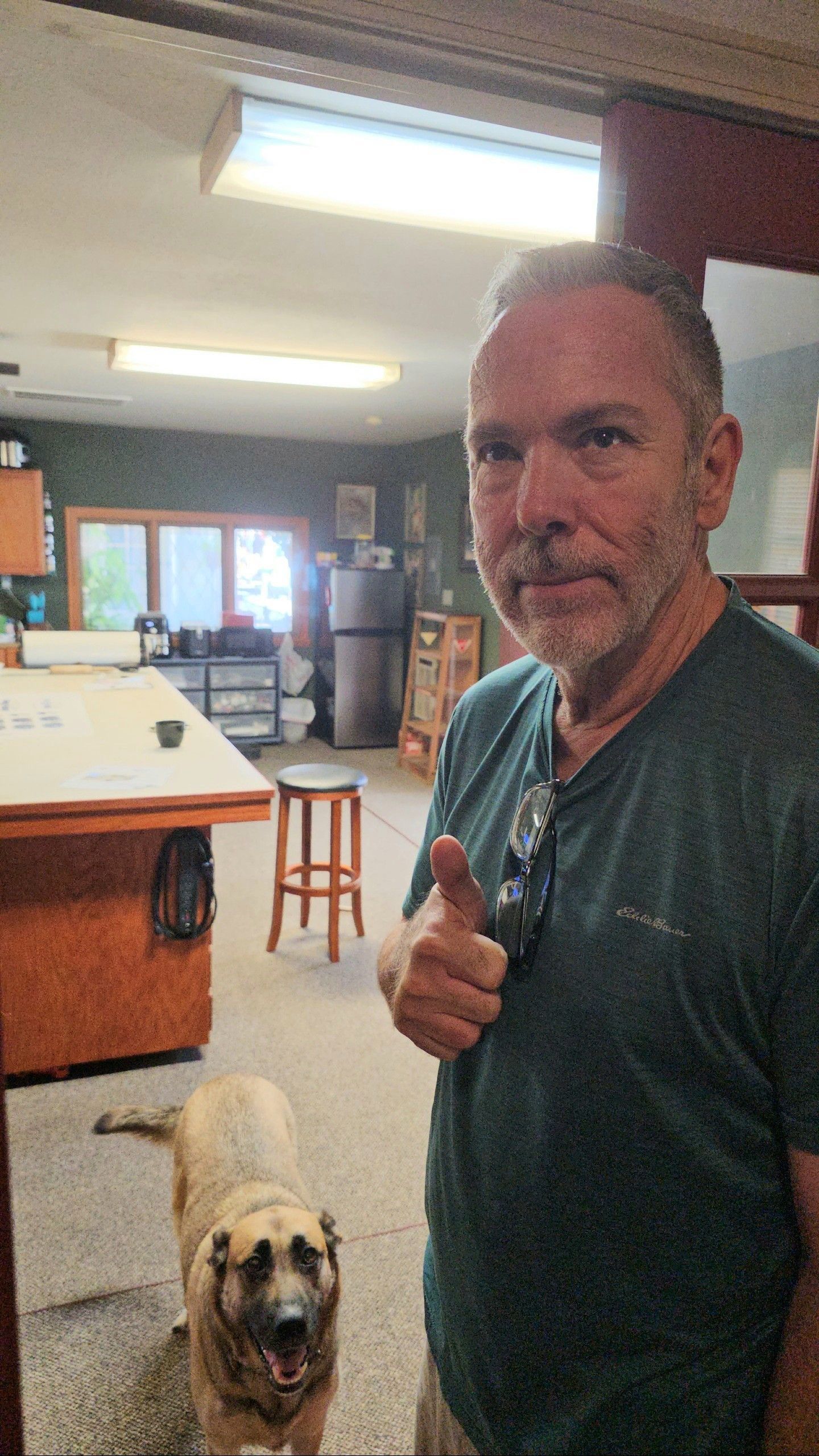 A man is standing next to a dog in a room and giving a thumbs up.