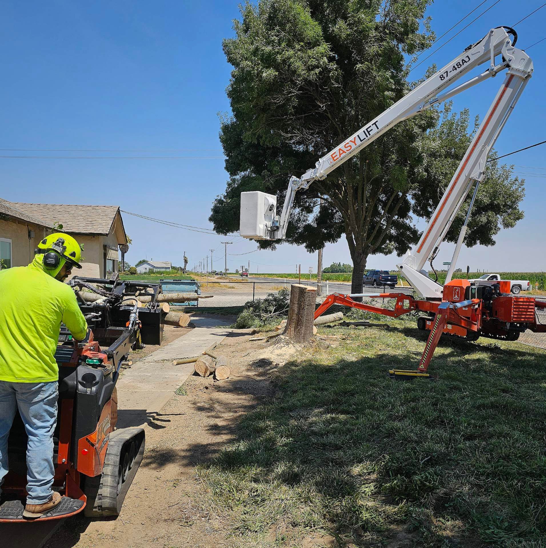 A man in a yellow shirt is using a crane to remove a tree stump.