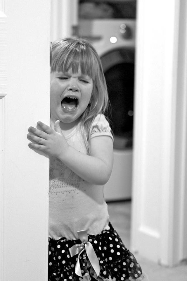 A little girl is crying behind a door in a black and white photo.