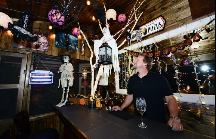 A man is sitting at a bar in a room decorated for halloween.