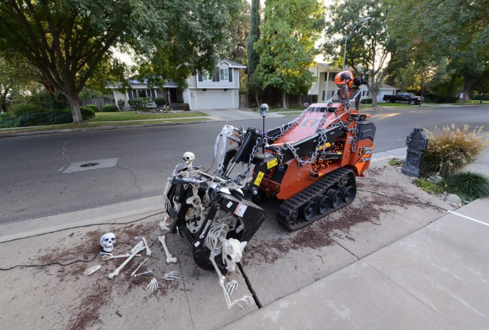 A skeleton is sitting on the sidewalk next to a machine.