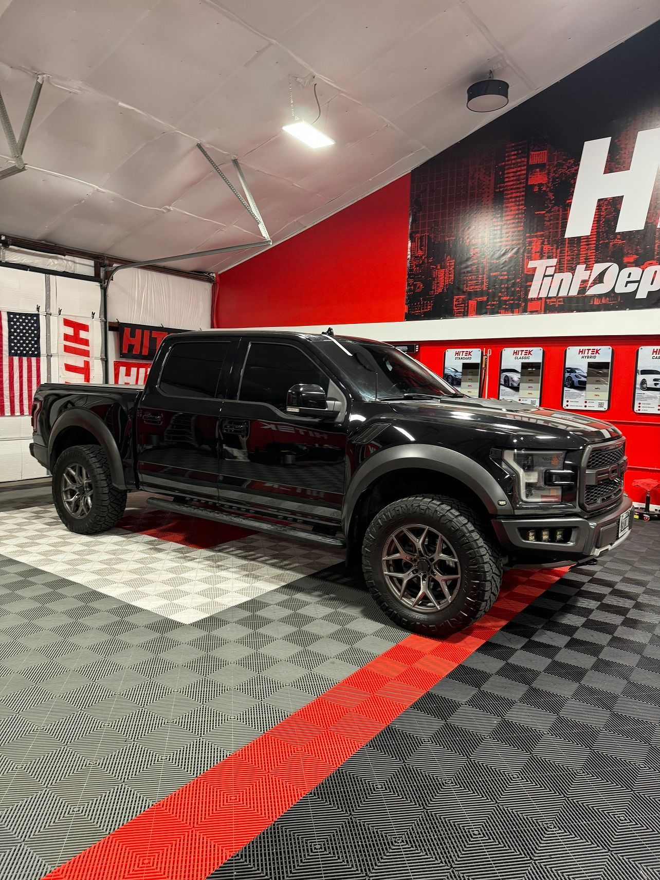 A black ford raptor is parked in a garage.